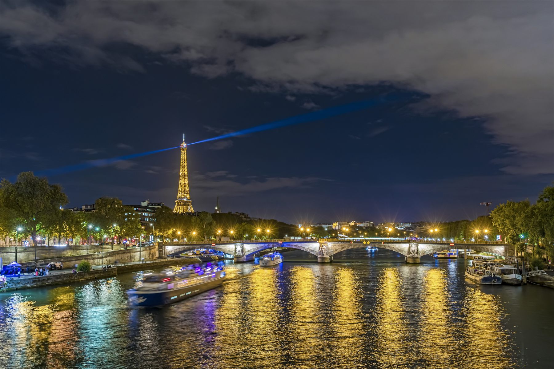 Boats on the Seine at night below the lit Eiffel Tower, Paris