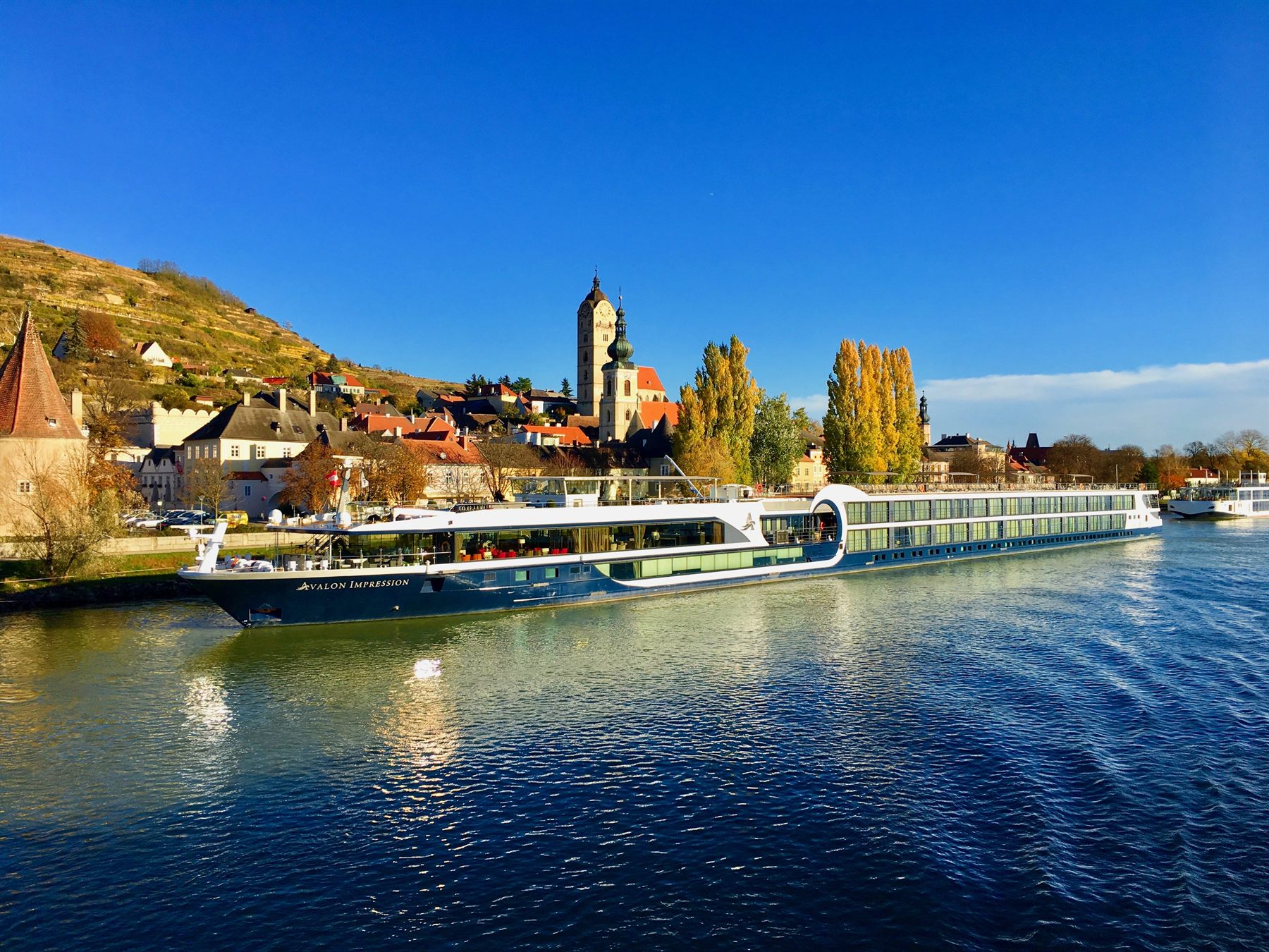 Avalon Impression moored below a vineyard hill and church tower on the Danube in autumn